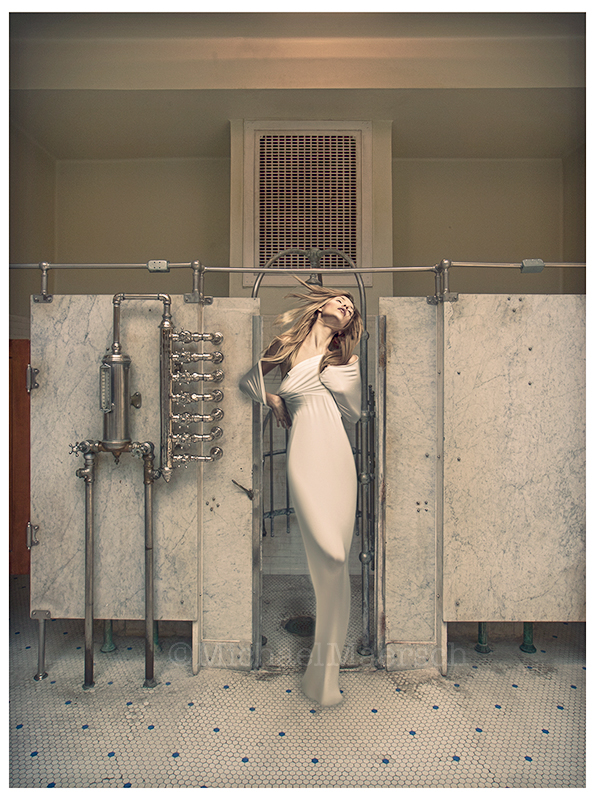 A tall, thin fashion model standing outside a Post-War era spa shower